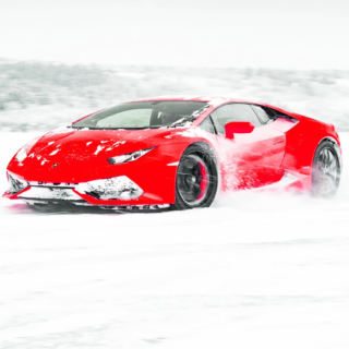 Roter Sportwagen driftet durch den Schnee, aufgewirbelte Schneefahnen und entblätterte Bäume im Hintergrund.
