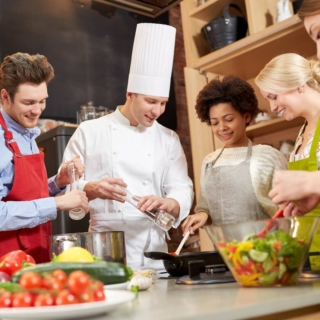 eine Gruppe von Kochkursteilnehmern kocht unter der Aufsicht eines erfahrenen Kochs