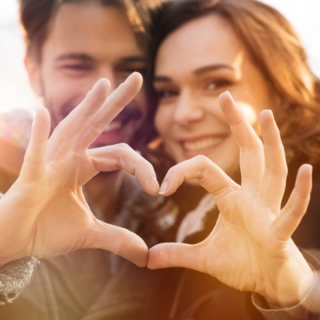 Ein Mann und eine Frau zeigen mit Fingerzichen ein Herz.