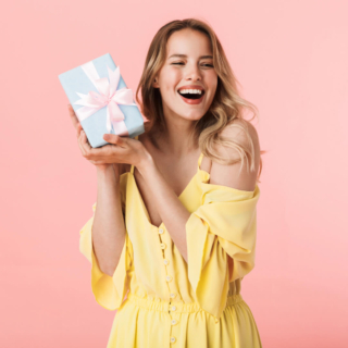 Eine Frau im gelben Kleid freut sich über ein Geschenk.
