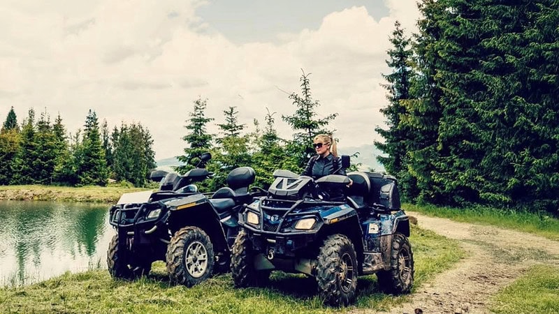 Eine Frau sitzt am Steuer eines Quads, umgeben von Wäldern und einem ruhigen See.