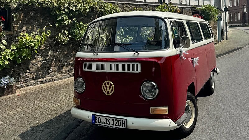 Roter mit Schleifen verzierter VW Bulli Parkt am Straßenrand.