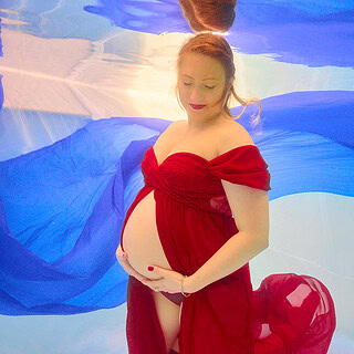 Eine schwangere Frau hält ihren Babybauch unter dem Wasser bei einem Unterwasser Babyshooting.