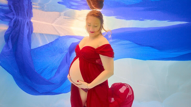 Eine schwangere Frau hält ihren Babybauch unter dem Wasser bei einem Unterwasser Babyshooting.