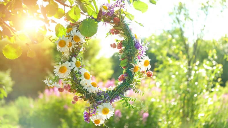 Ein großer Blumenkranz hängt von einem Zweig auf einer Wiese.