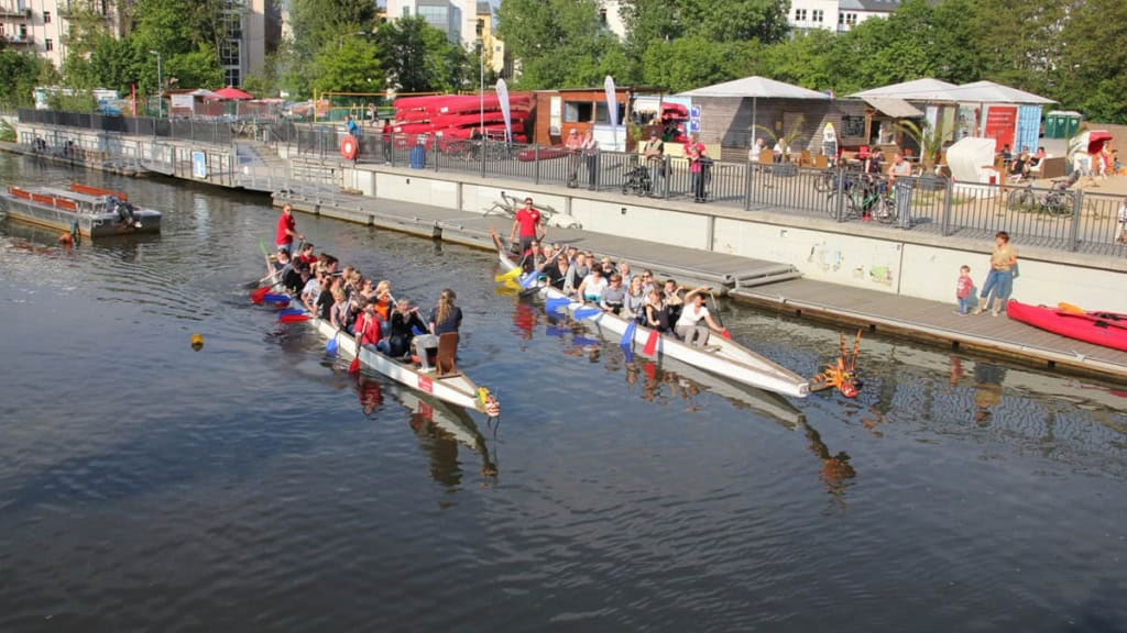 Drachenboote an einer Anlegestelle mit Ruderern im Sonnenschein.