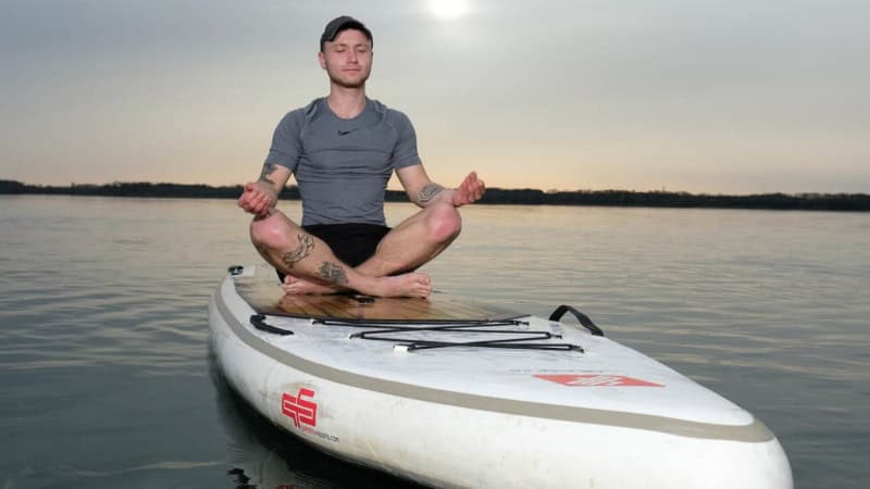 ein Mann meditier auf seinem stand up paddle auf einem See