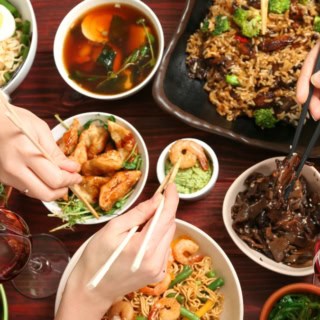 Verschiedene asiatische Gerichte stehen auf einem Tisch von dem sich Menschen mit Stäbchen bedienen.