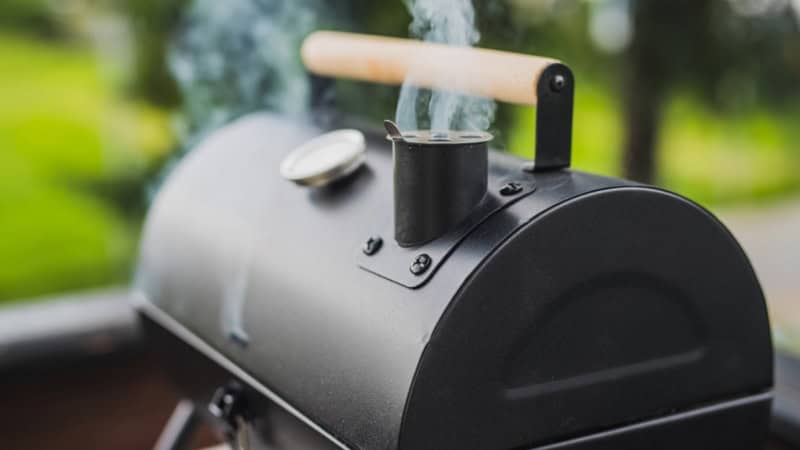 Ein Smoker aus dessen Schornstein Dampf steigt.