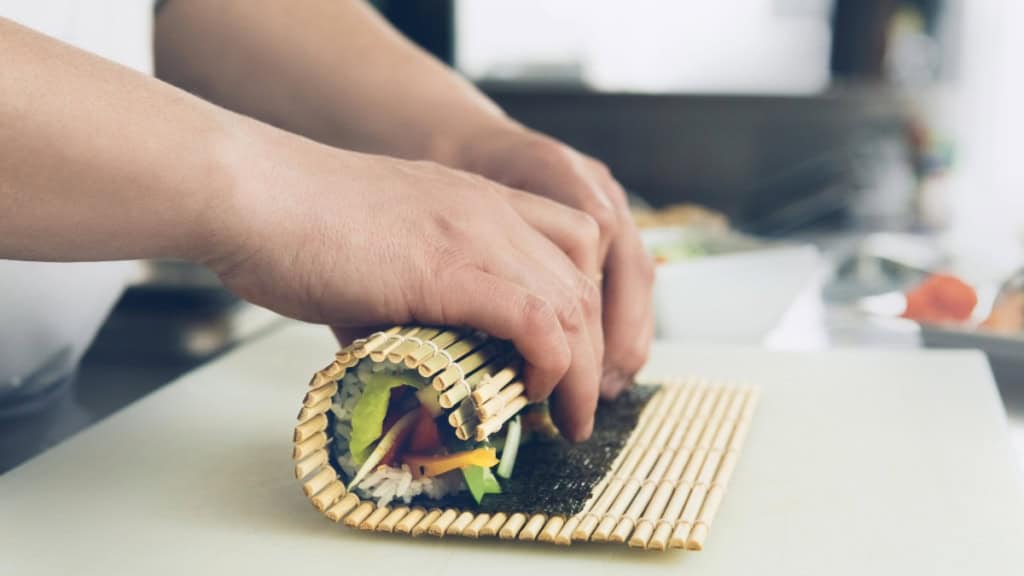 Sushi wird in einer Sushi Rollmatte geformt.