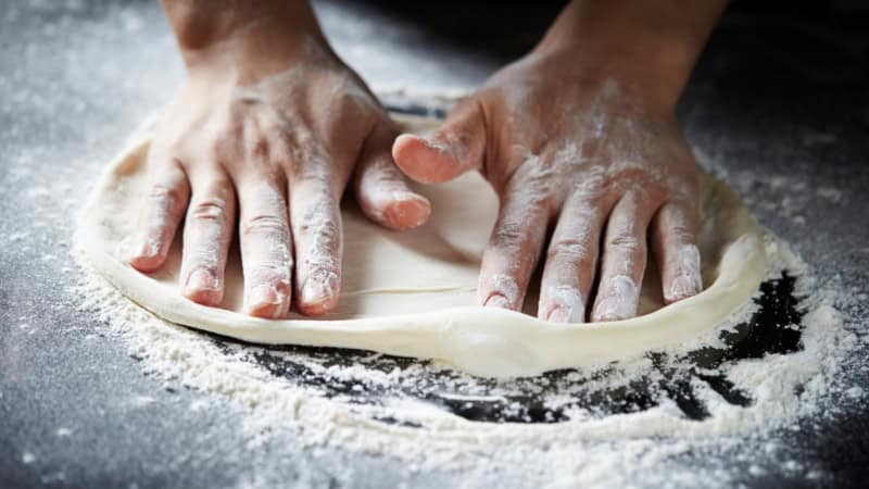 Ein Pizza Teig wird in Mehl geformt und geknetet.