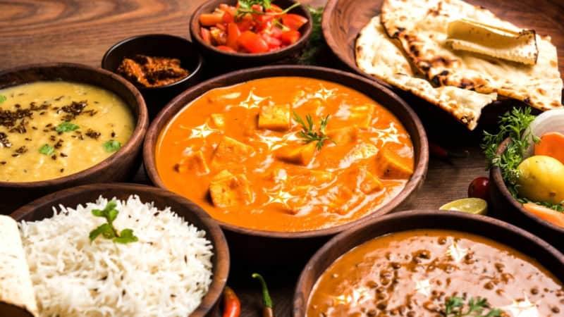 Indisches Fladenbrot, Chicken Curry und Reis stehen gemeinsam mit weiteren indischen Gerichten auf einem Tisch.