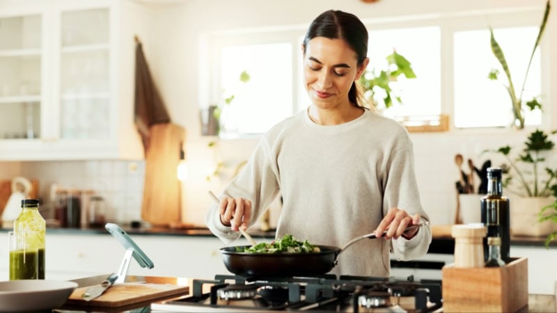 Eine Frau nimmt an einem Online Kochkurs teil und brät veganes Essen an.