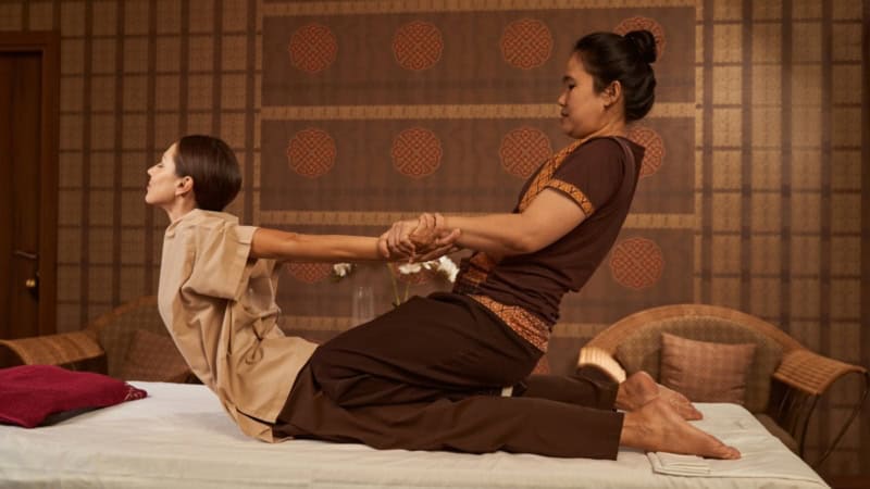 Mit Dehnbewegungen werden bei einer Frau Verspannungen gelöst - Thai Ganzkörpermassage.