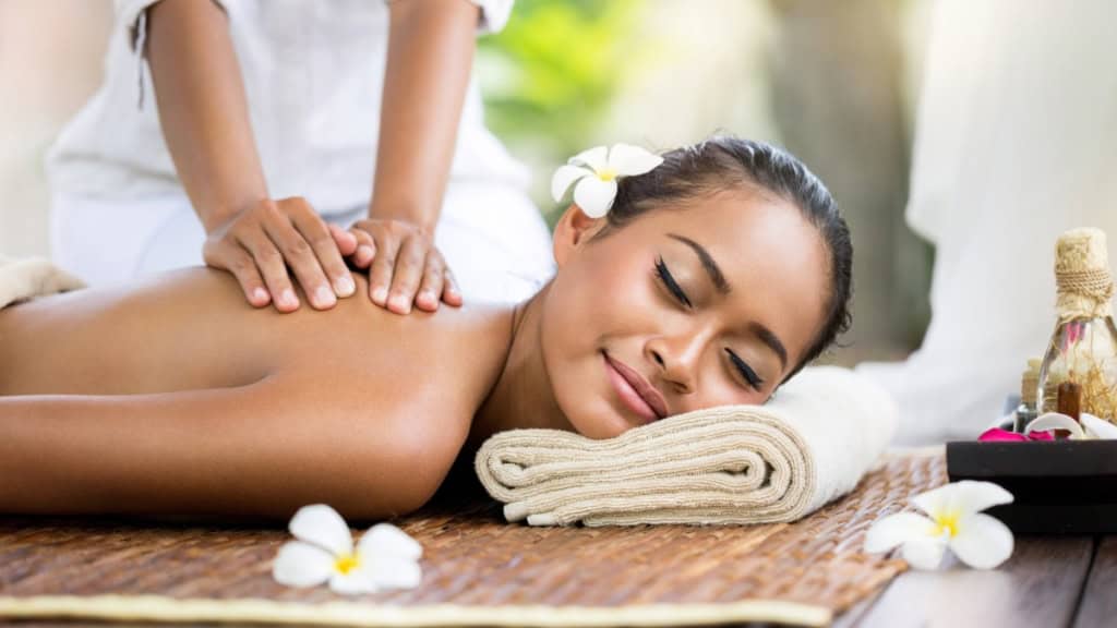Eine Frau liegt auf einer Bodenmatte. Dabei erhält sie eine Thai Rückenmassage.