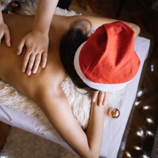 Eine Frau mit einer Weihnachtsmütze bekommt eine wohltuende Rückenmassage.