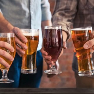 Vier Männer stoßen mit jeweils einem gefüllten Glas Bier an.
