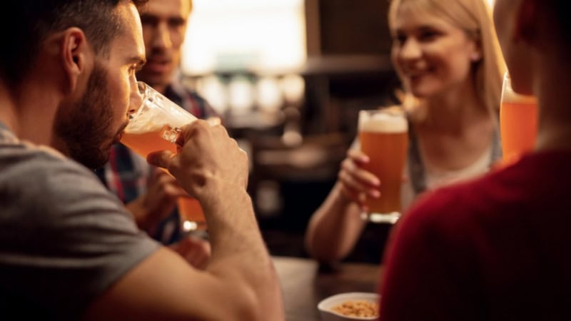 Vier Freunde sitzen zusammen an einem Tisch und trinken Bier aus Biergläsern.