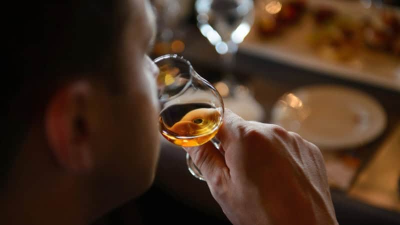Mann sitzt an einem Esstisch und verkostet Whiskey aus einem Glas.