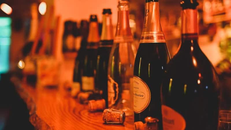Verschiedene orange beleuchtete Champagnerflaschen stehen aufgereiht auf einem Bartresen.