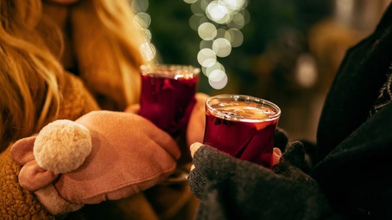 Nahaufnahme eines Paares, das frischen Glühwein in Gläsern in der Hand hält.