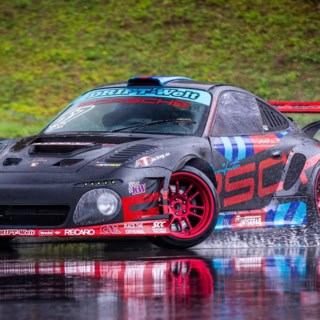 Ein schwarzes Sportauto von Porsche driftet über nassen Asphalt auf dem Nürburgring.