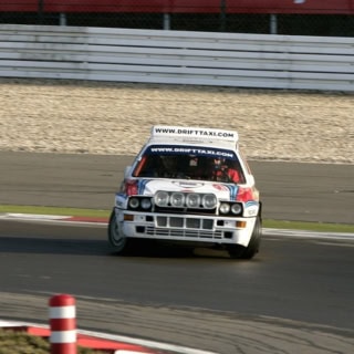 Ein weißes Auto driftet in einer Kurve der Rennstrecke des Nürburgrings.