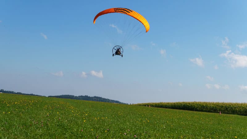 Trike ist in der Luft und gerade bei der Landung. Unten Wiese oben Himmel.