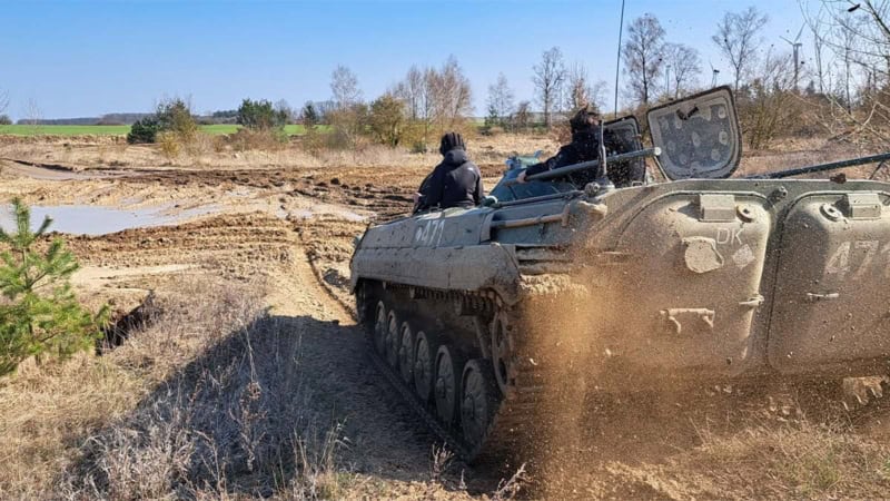 Ein Panzer von hinten der durch Matsch fährt. Der Matsch spritzt hinter dem Panzer hoch.