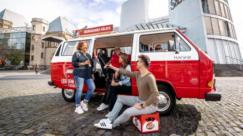 Ein Vw Bulli der vor dem Schokoladenmuseum in Köln parkt. Die Bulli Tour Teilnehmer stoßen gemeinsam auf ein kölsch an.