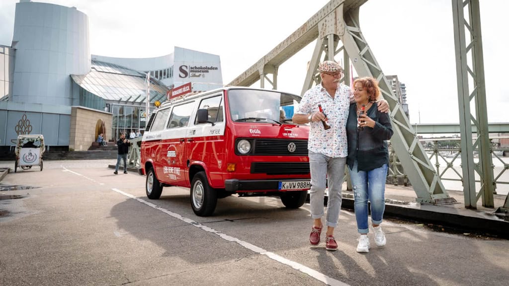 Ein Paar steht vor einem VW Bulli der vor dem Schokoladenmuseum im Köln steht.