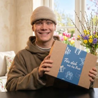 Ein Mann hält voller Freude die Geschenkbox der Erlebnisfabrik, die er zu Ostern geschenkt bekommen hat.